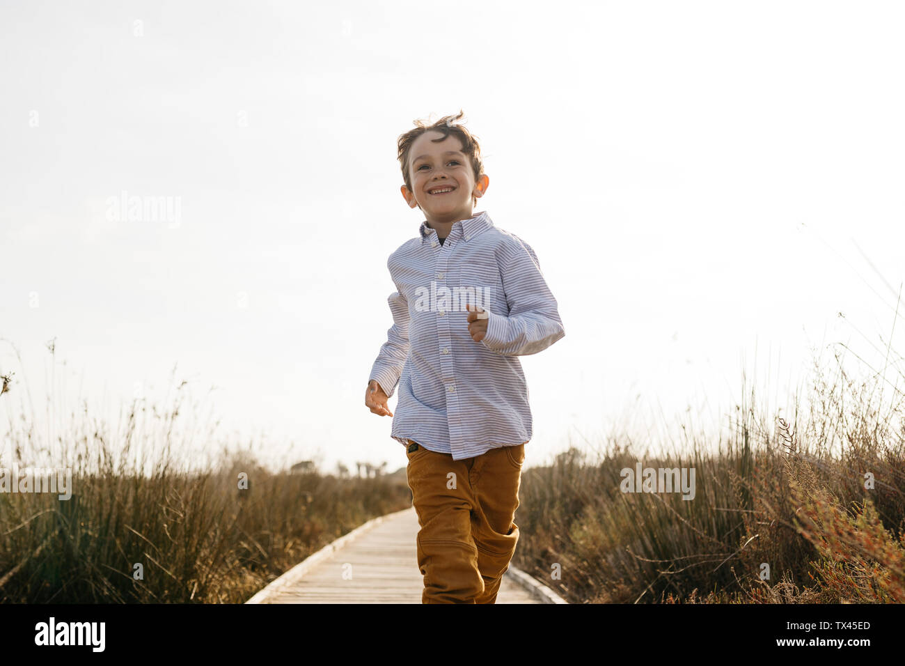 Portrait of happy little boy running on boardwalk Stock Photo