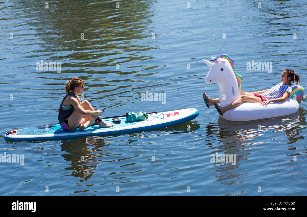 Woman paddleboarder paddle boarder and inflatable unicorn inflatable relaxing on Dorset Dinghy Day at River Stour, Iford, Dorset UK in June Stock Photo