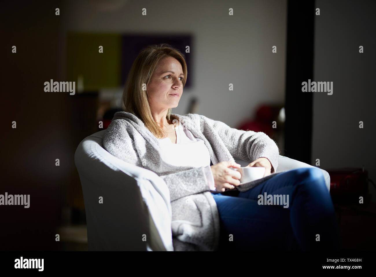 Woman sitting at home, relaxing in arm chair Stock Photo