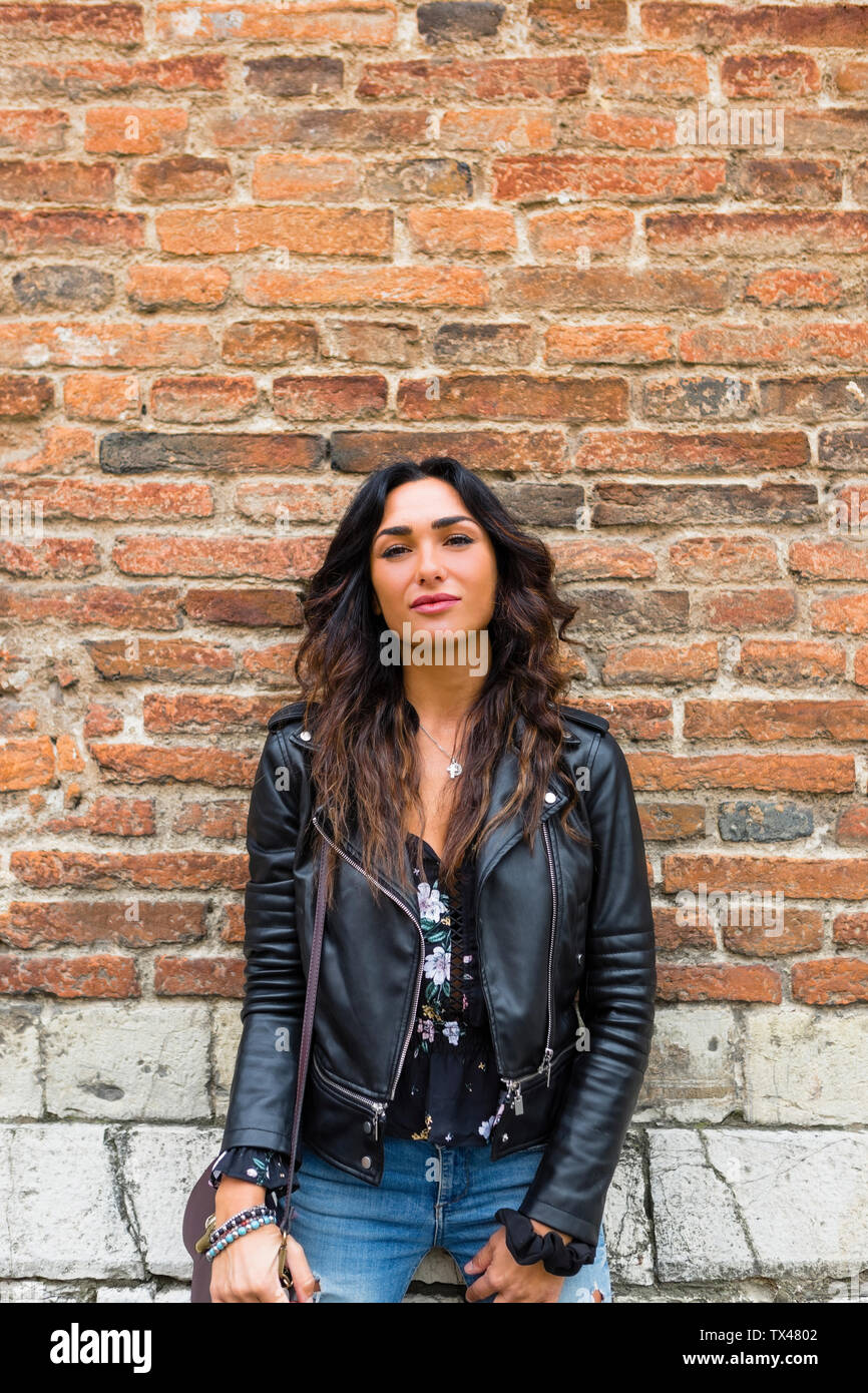 Portrait of young woman wearing black leather jacket, brick wall Stock ...