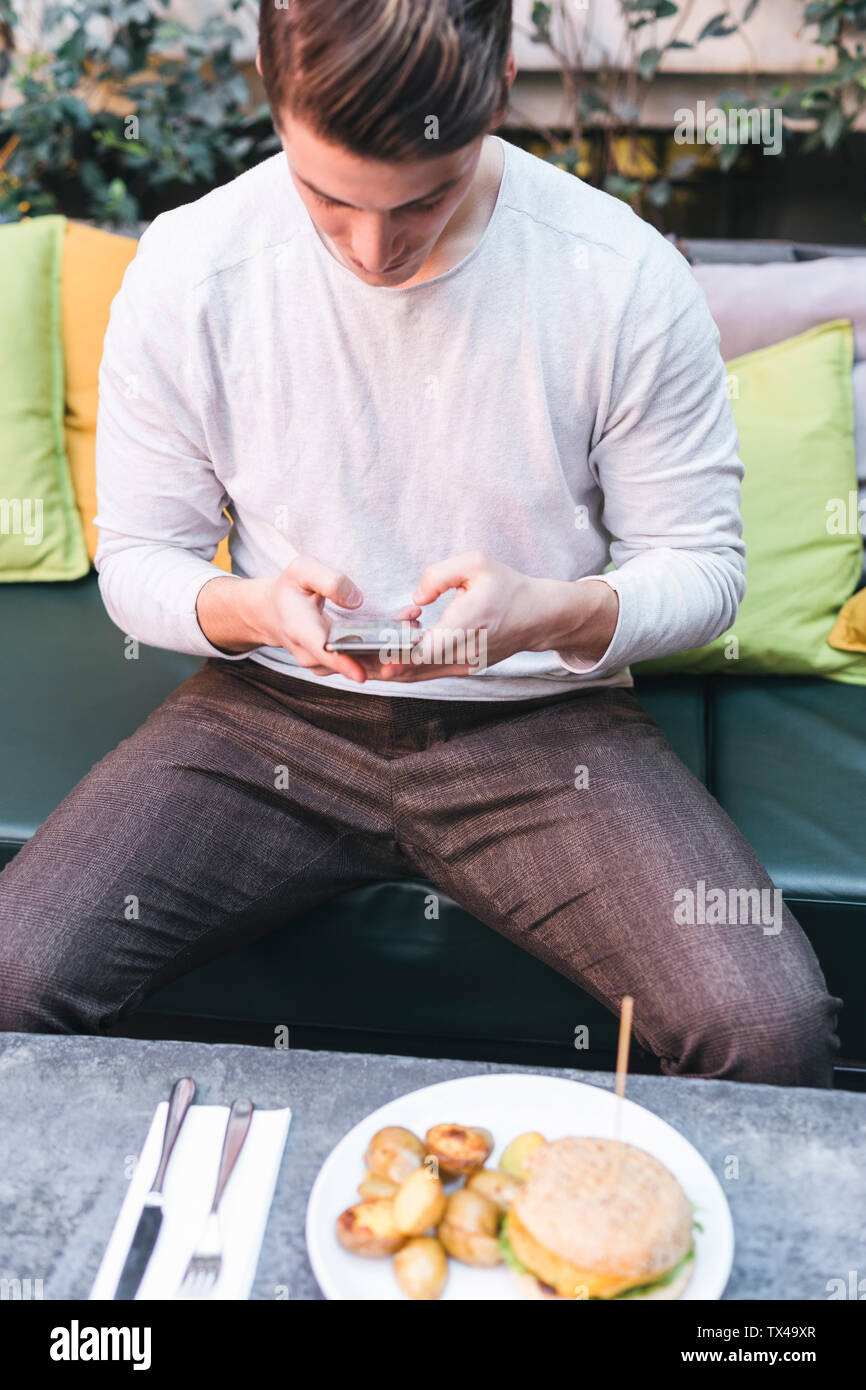 Young man sitting on couch in a restaurant using cell phone during