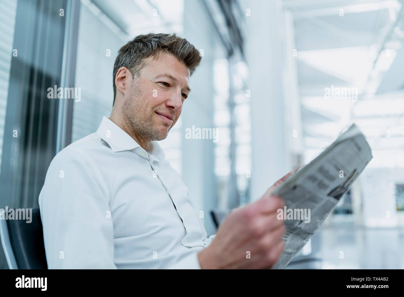 Businessman sitting in waiting area reading newspaper Stock Photo