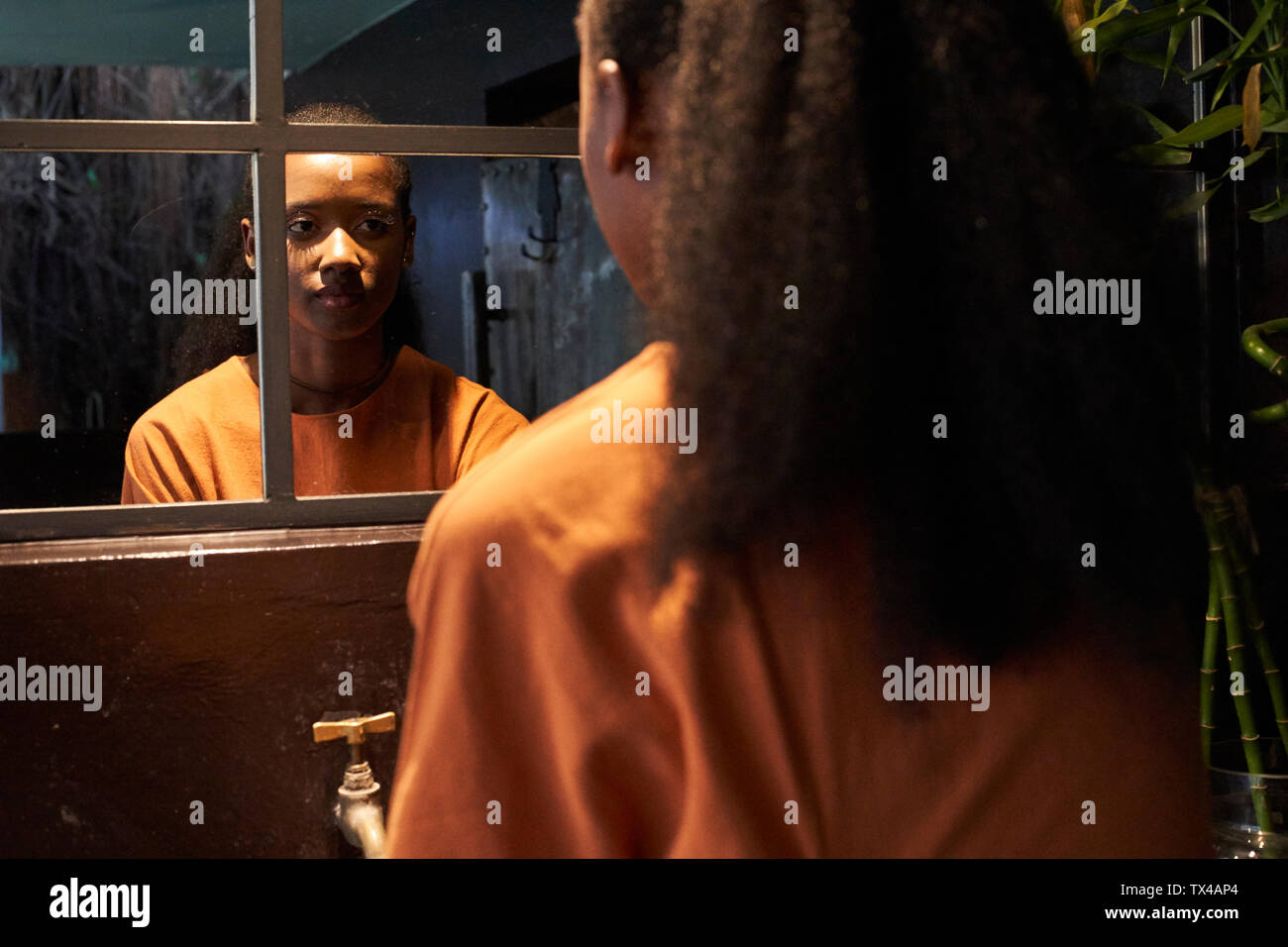 Young woman looking in bathroom mirror Stock Photo - Alamy