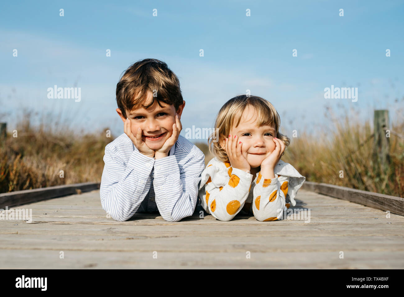 Portrait of boy and his little sister lying side by side on boardwalk Stock Photo