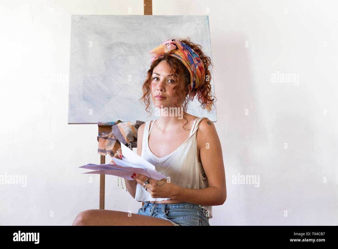 Portrait of young female painter in art studio next to empty canvas Stock Photo