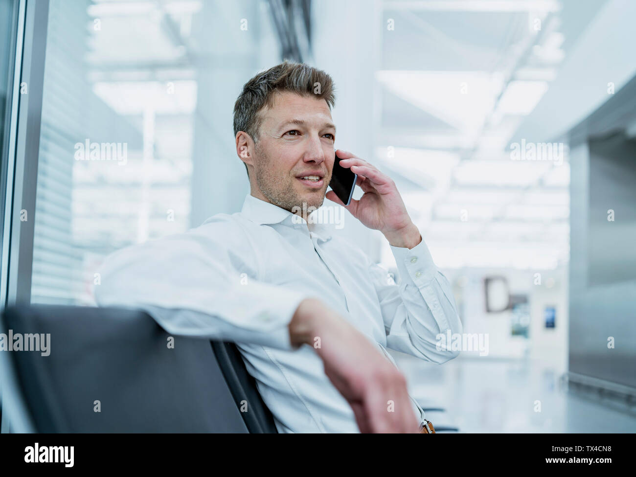 Businessman sitting in waiting area talking on cell phone Stock Photo