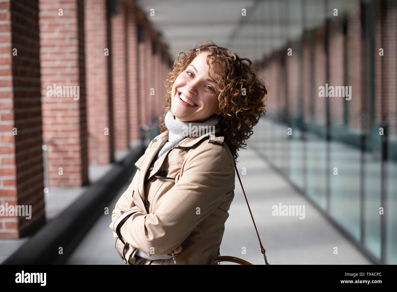 Portrait of happy woman with curly hair wearing beige trenchcoat and turtleneck pullover Stock Photo