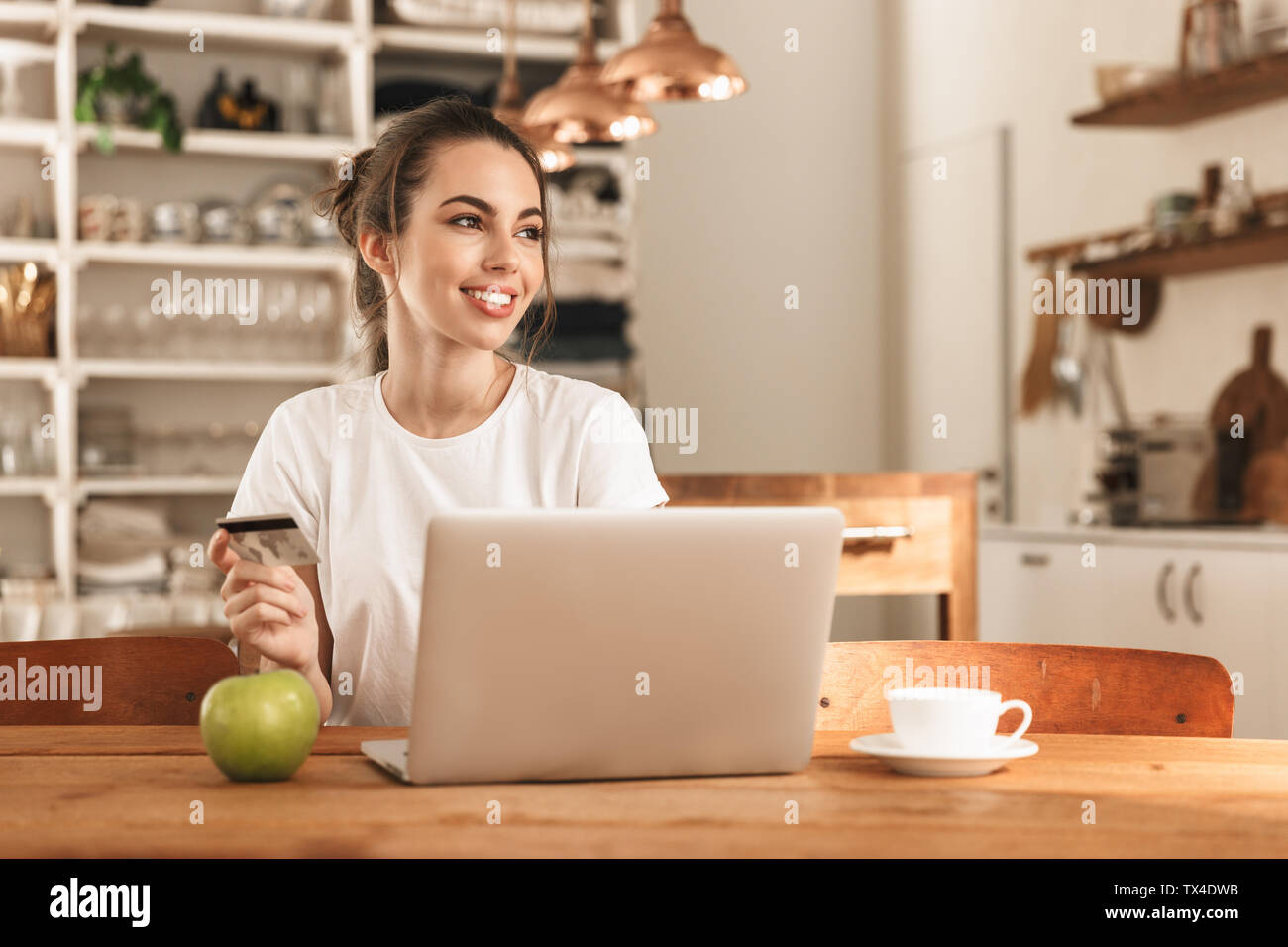 Image of a beautiful young student girl with apple indoors using laptop ...