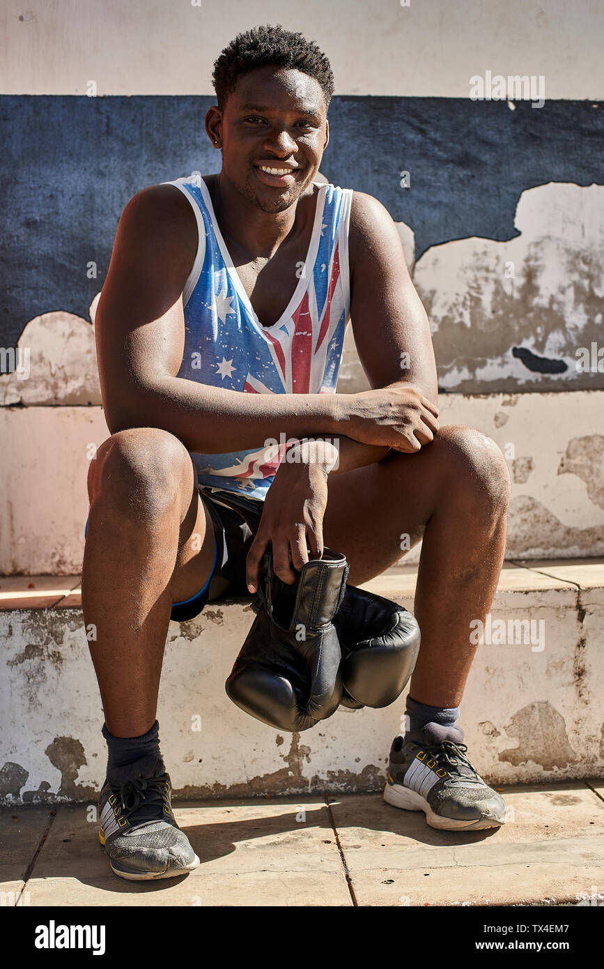 Portrait of smiling boxer with his boxing gloves sitting outdoors after training Stock Photo
