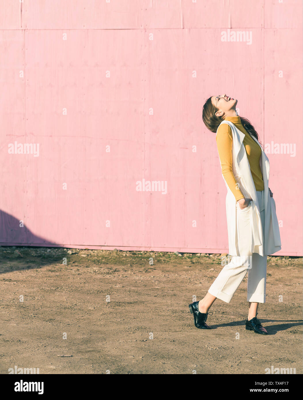 Happy young woman standing in front of pink wall Stock Photo - Alamy
