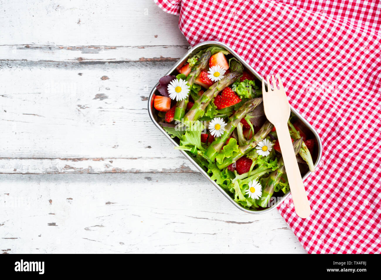 Lunchbox with green salad, green asparagus, strawberries and daisies Stock Photo