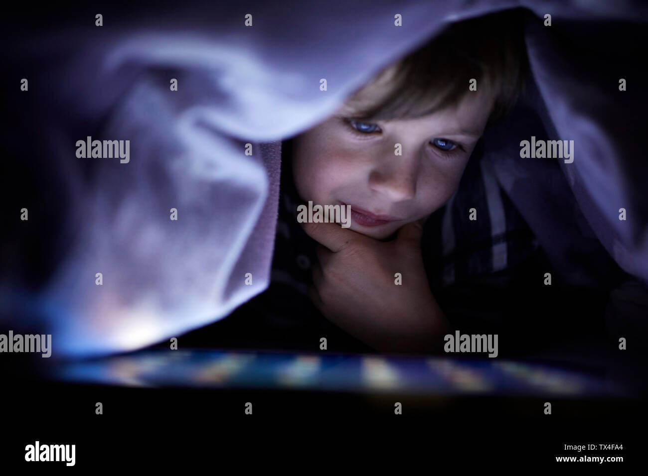 Little boy playing secretly with his digital tablet, hidden under blanket Stock Photo