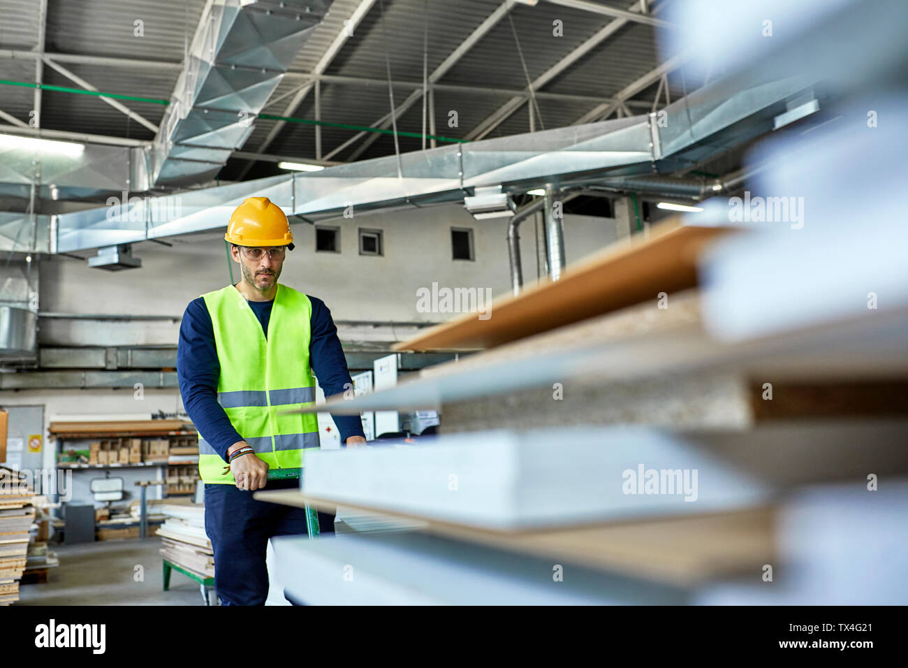 Worker pulling pallet jack with wooden boards in factory Stock Photo
