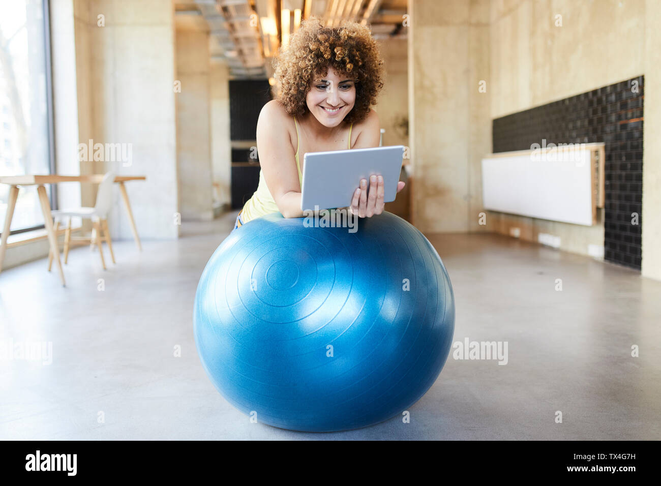 Smiling woman using tablet on fitness ball in modern office Stock Photo