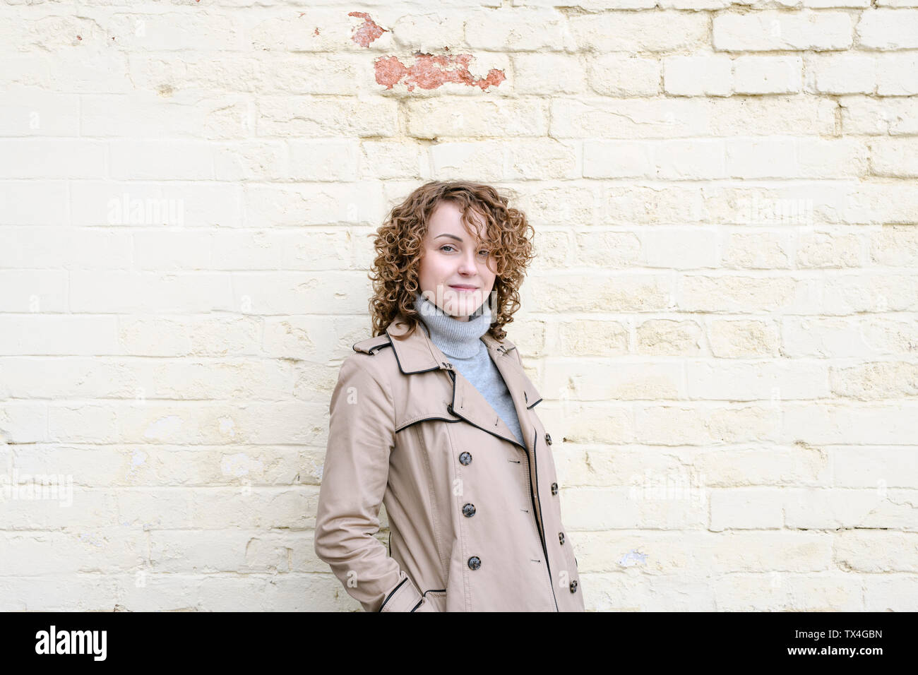 Portrait of smiling woman with curly hair wearing beige trenchcoat Stock Photo