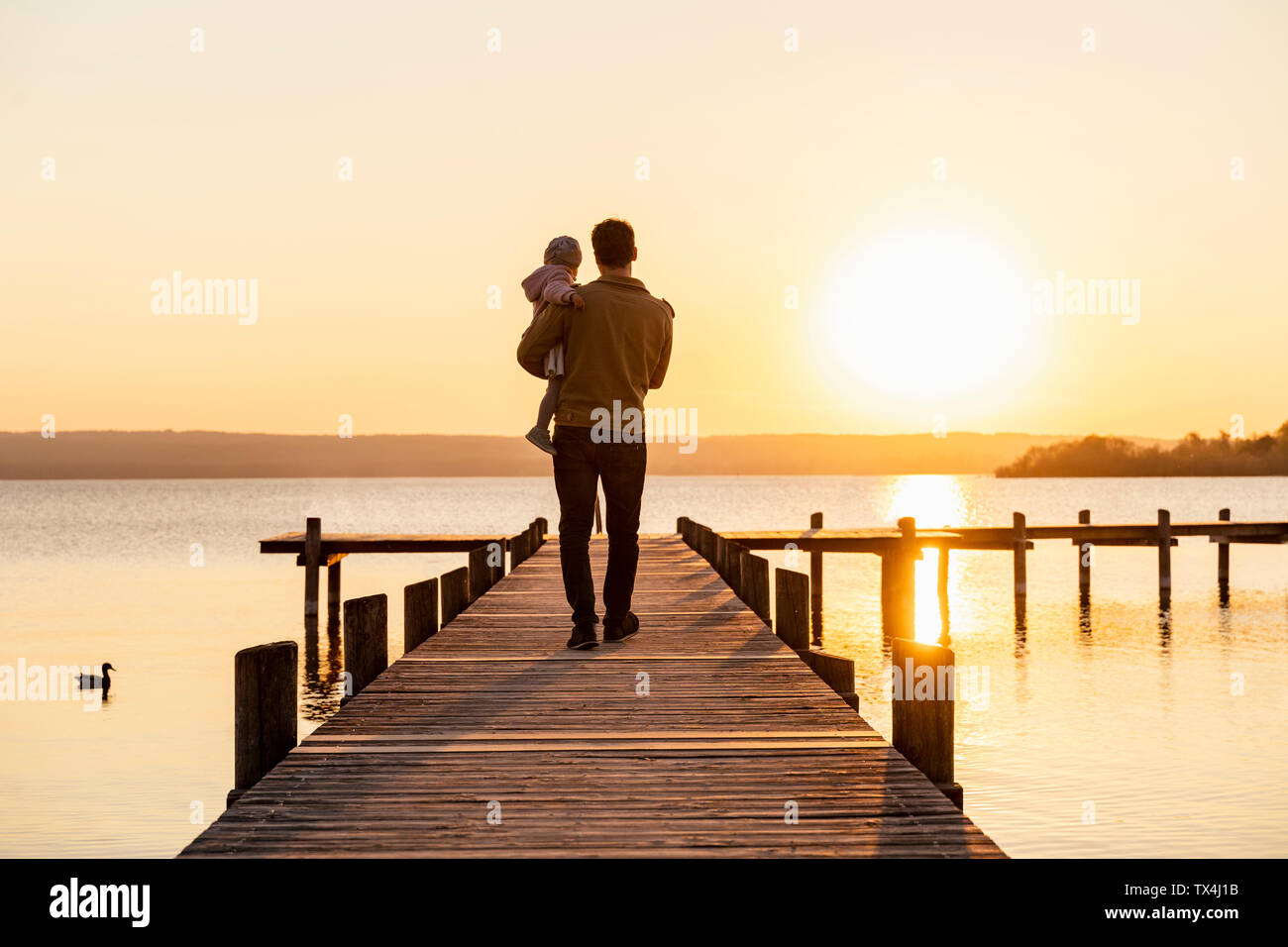 Germany, Bavaria, Herrsching, father carrying daughter on jetty at sunset Stock Photo