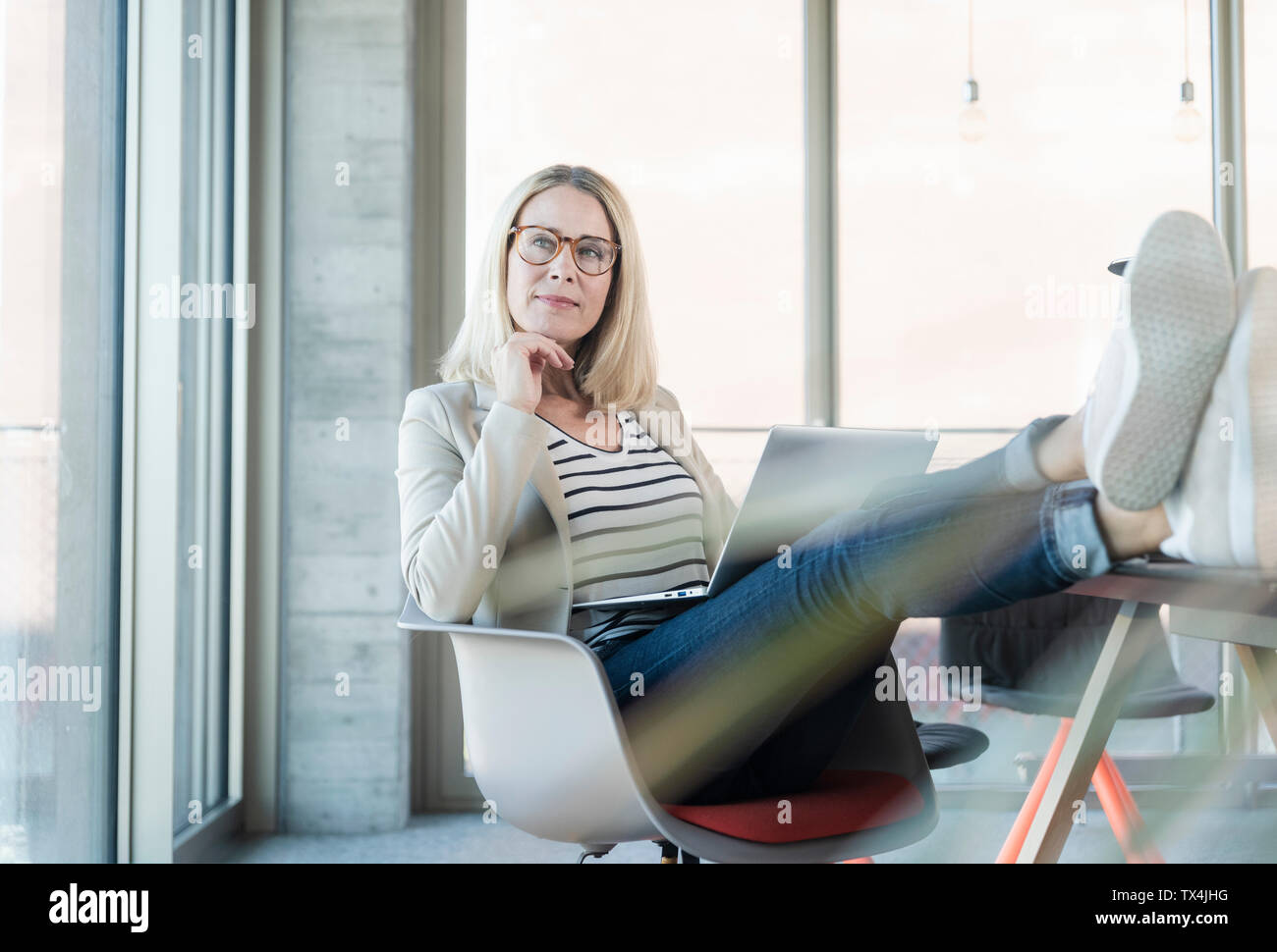 Relaxed businesswoman using laptop in office with feet up Stock Photo