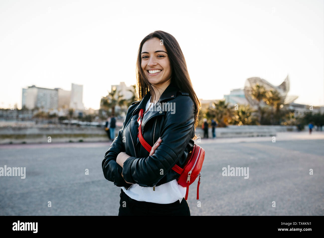 Happy young woman with a red hip bag with arms crossed looking at camera Stock Photo