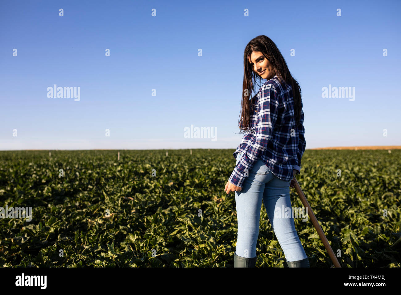 Young woman farmer with hoe on field, rear view Stock Photo