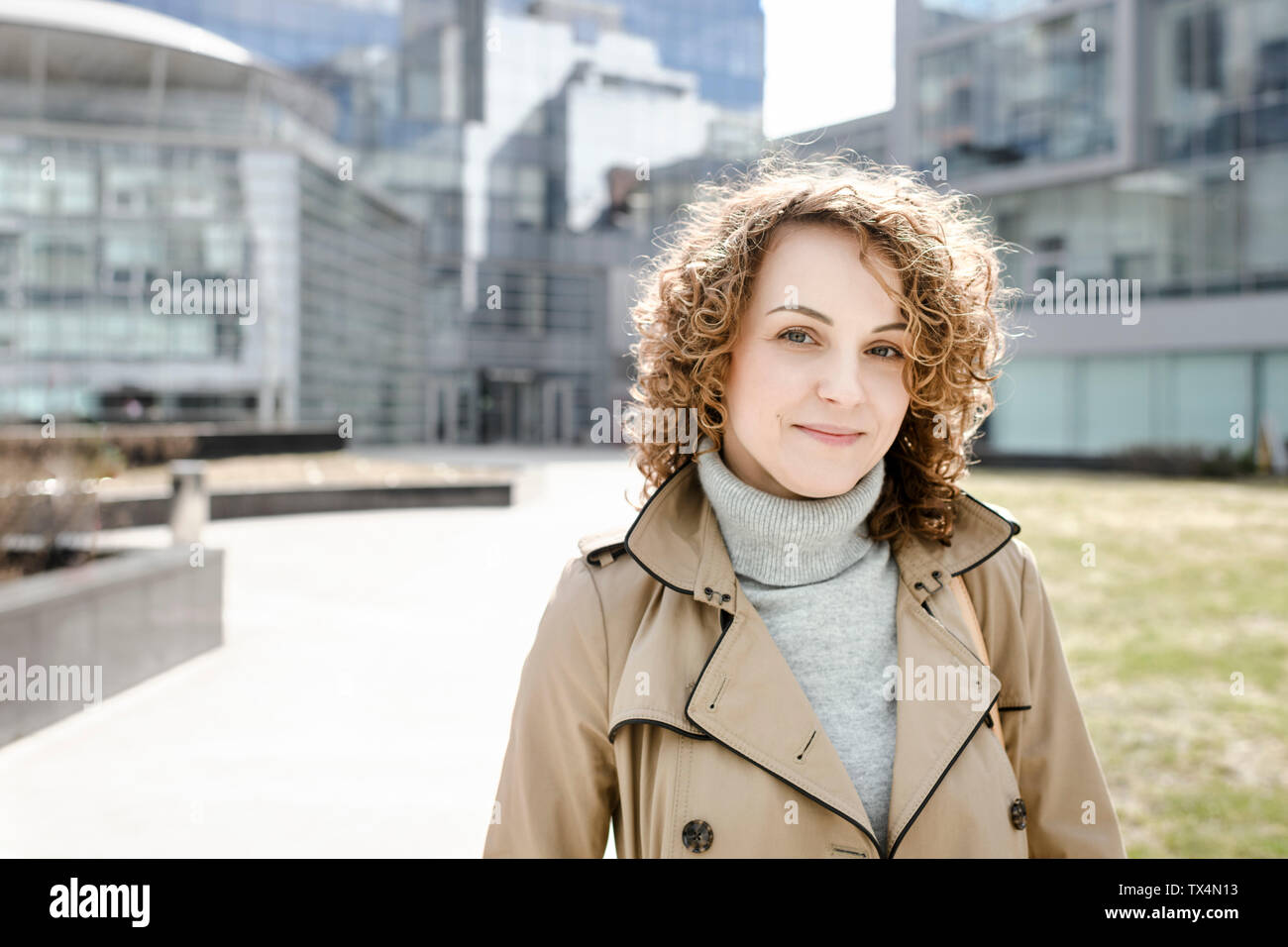 Portrait of smiling woman with curly hair wearing beige trenchcoat and turtleneck pullover Stock Photo