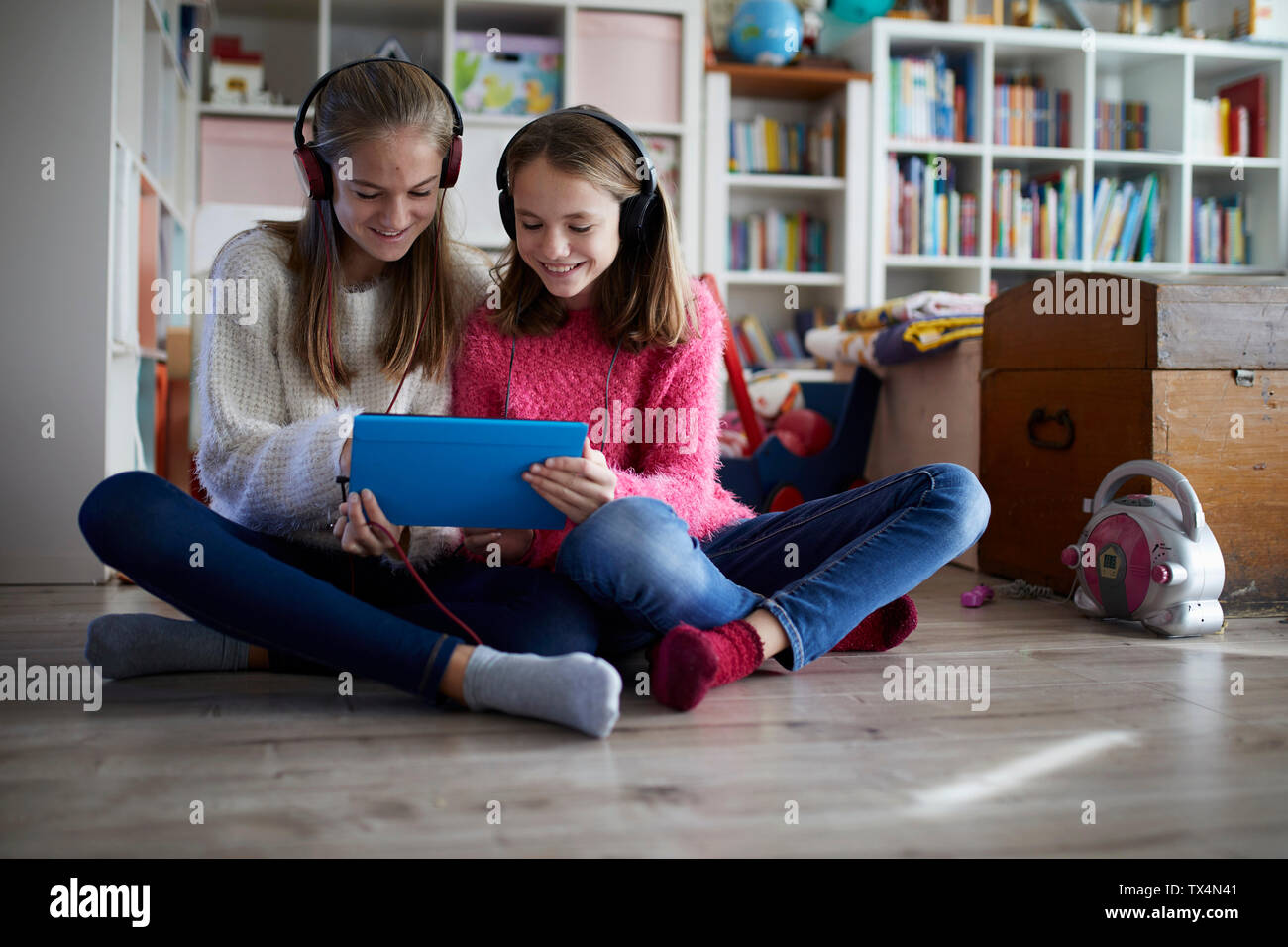 Siblings playing at home with their digital tablets, sitting on ground Stock Photo