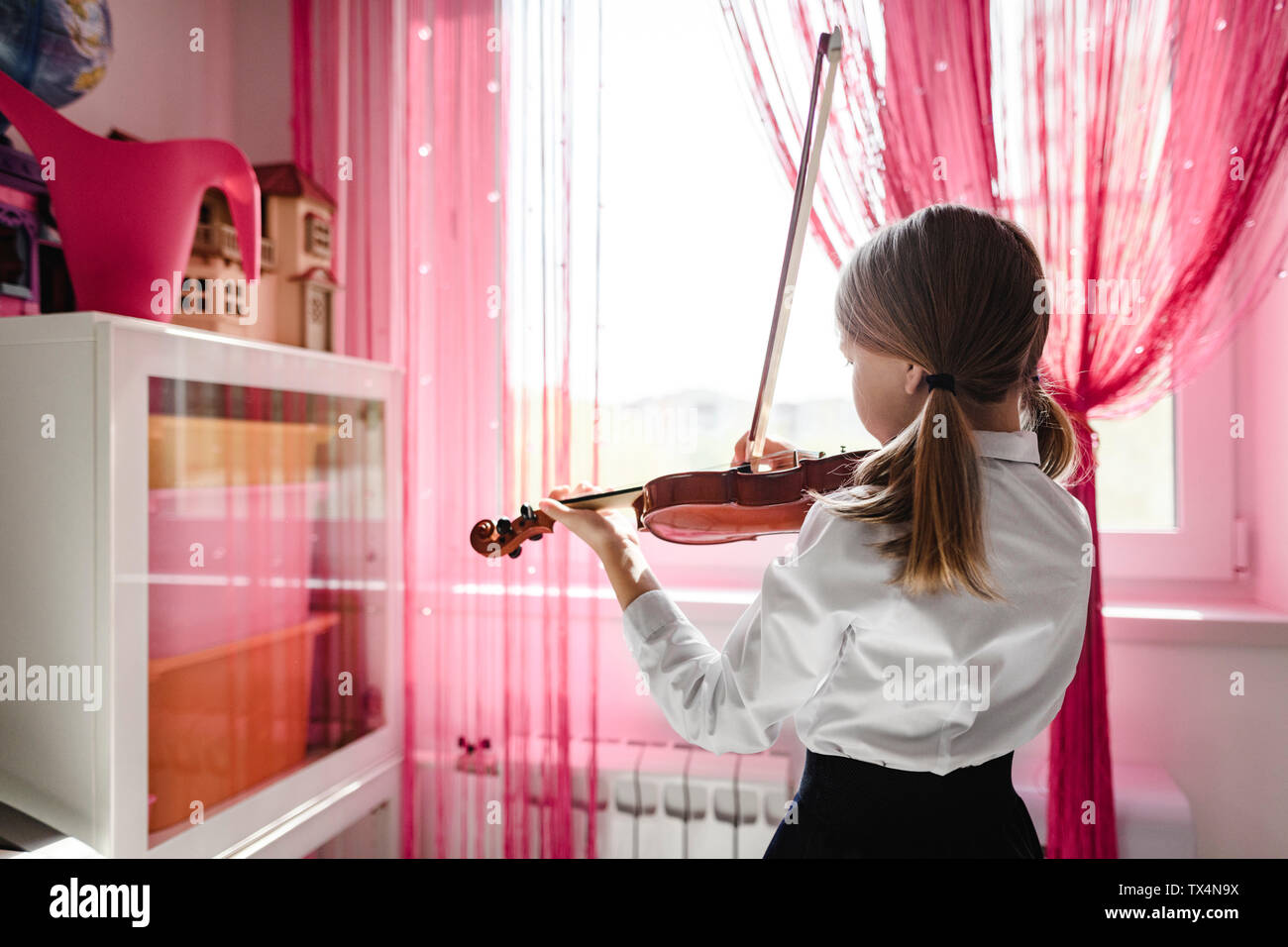 Girl playing violin at the window at home Stock Photo