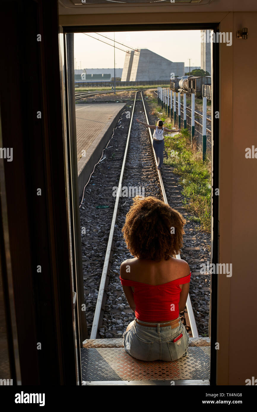 Woman sitting at the back door of a train looking at a woman on the tracks Stock Photo