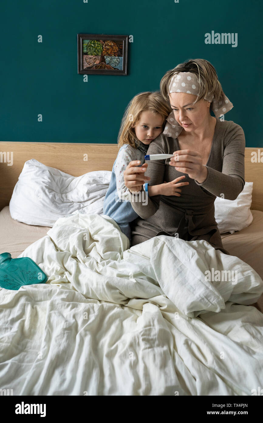 Mother taking temperature of sick daughter lying in bed Stock Photo