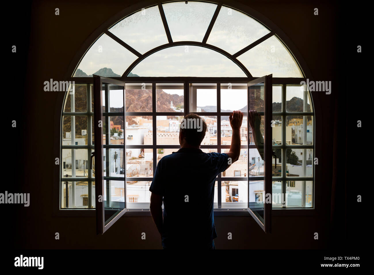 Man standing looking out of open window, Mutrah, Oman Stock Photo
