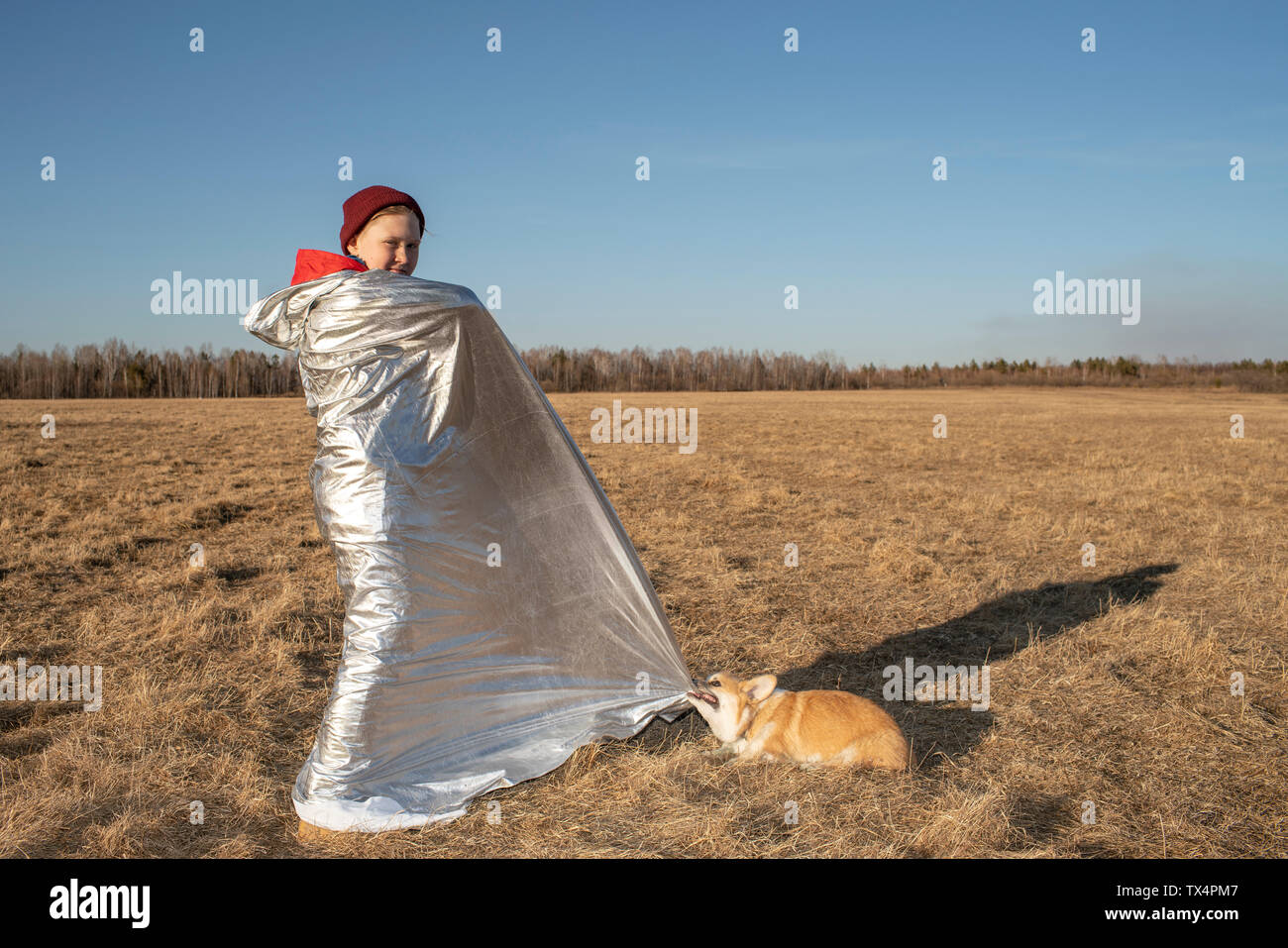 Boy wrapped up in superhero costume with dog in steppe landscape Stock Photo