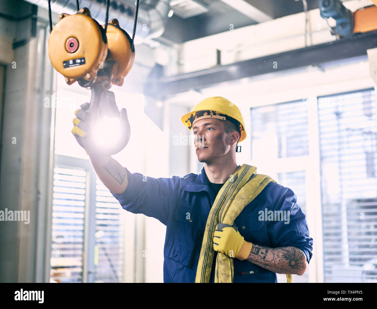 Industrial worker fixing hoist sling on indoor crane Stock Photo