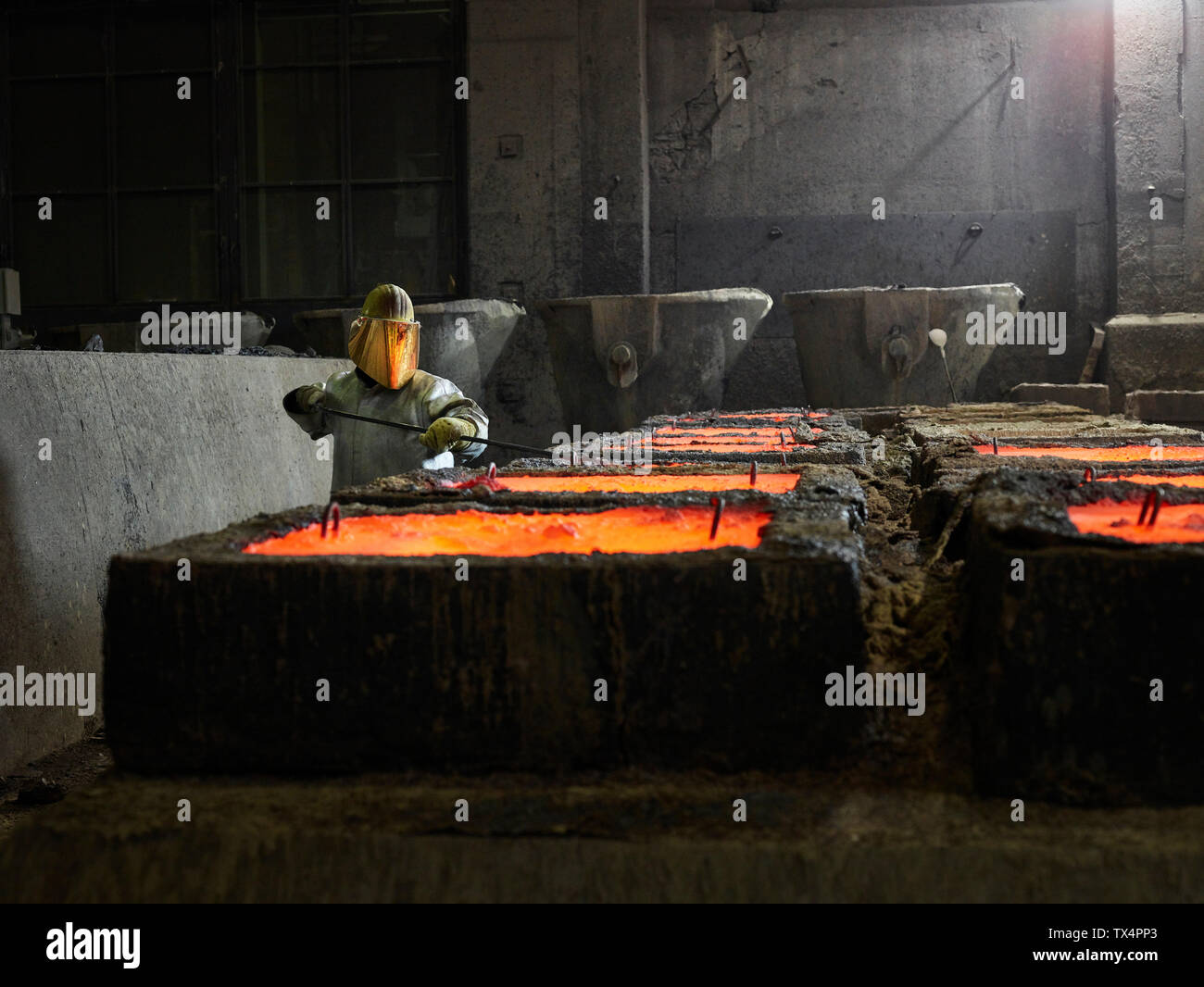 Industry, worker checking liquid copper in casting moulds with pliers Stock Photo