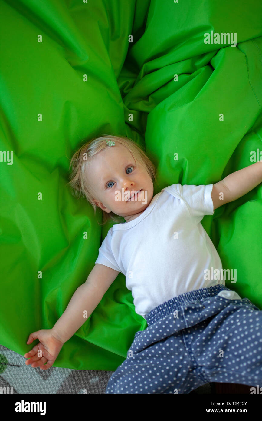 Portrait of little girl lying on green blanket in children's room Stock Photo