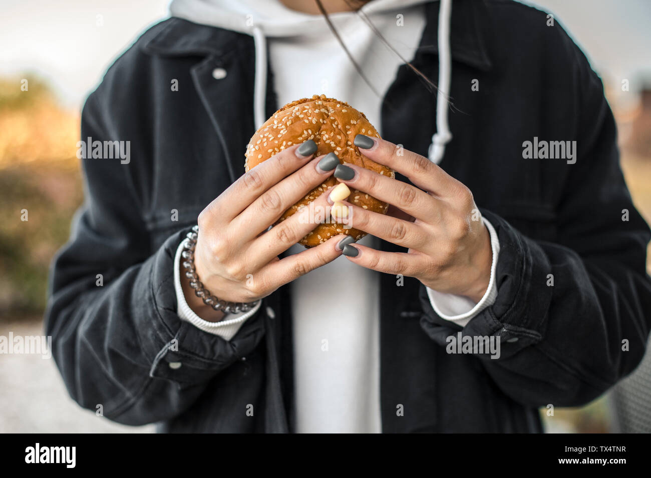 Hands of young woman with painted nails holding a hamburger, close-up Stock Photo
