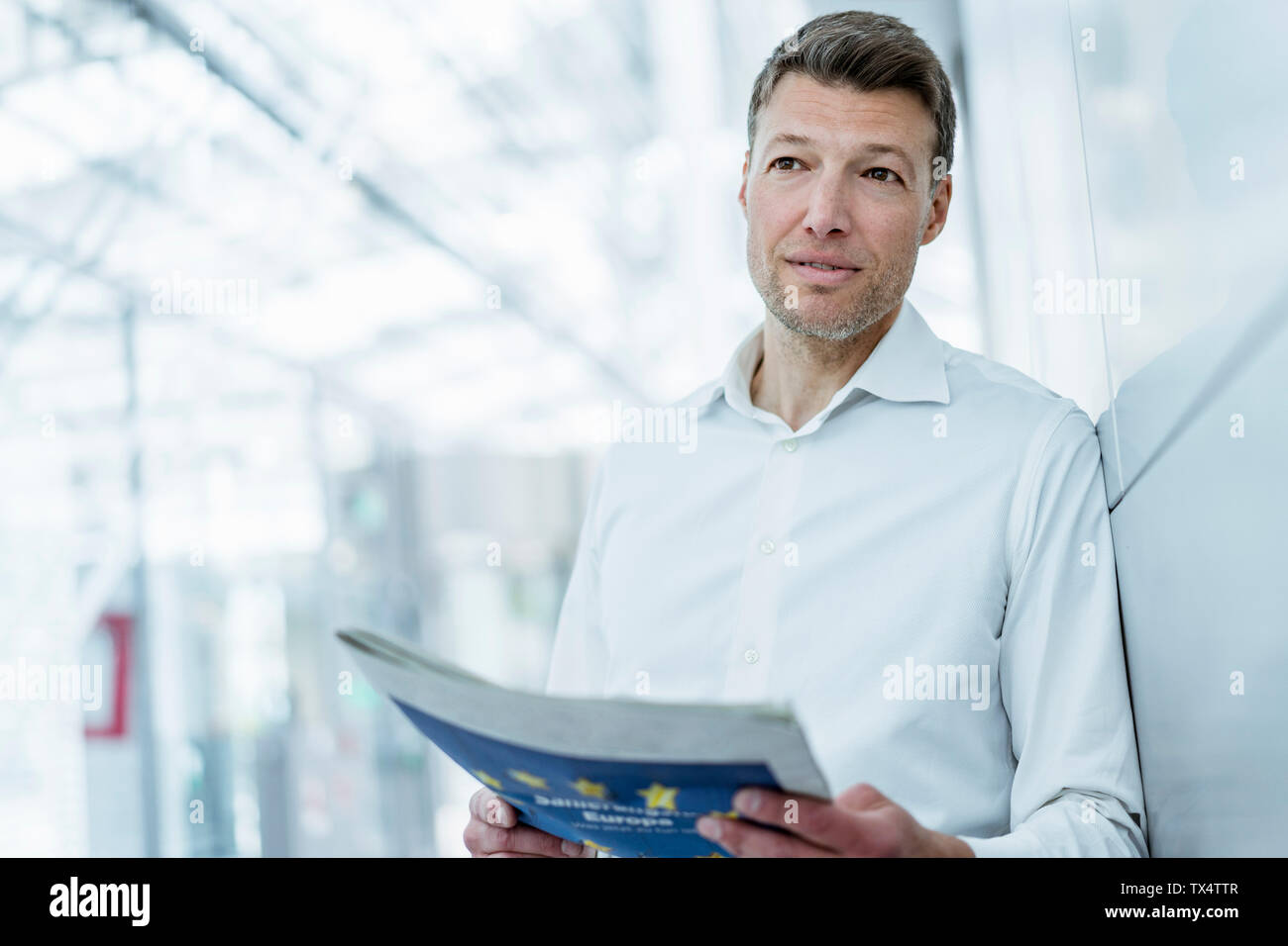 Businessman leaning against a wall reading newspaper Stock Photo