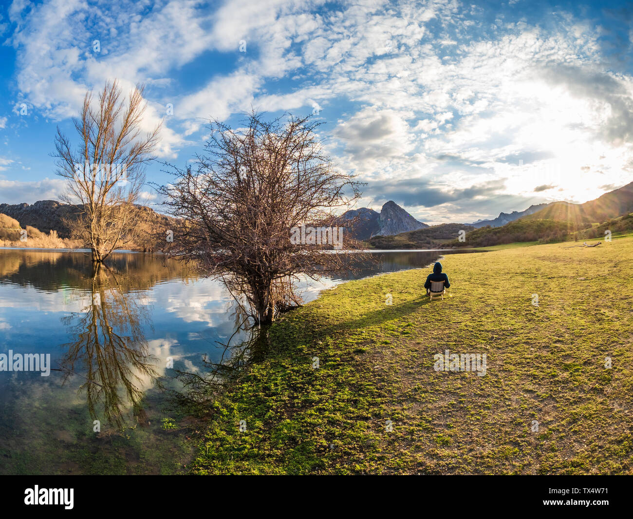 Spain, Asturias, Camposolillo, Cantabrian Mountains, senior man sitting at seashore of Porma reservoir enjoying the sunshine Stock Photo