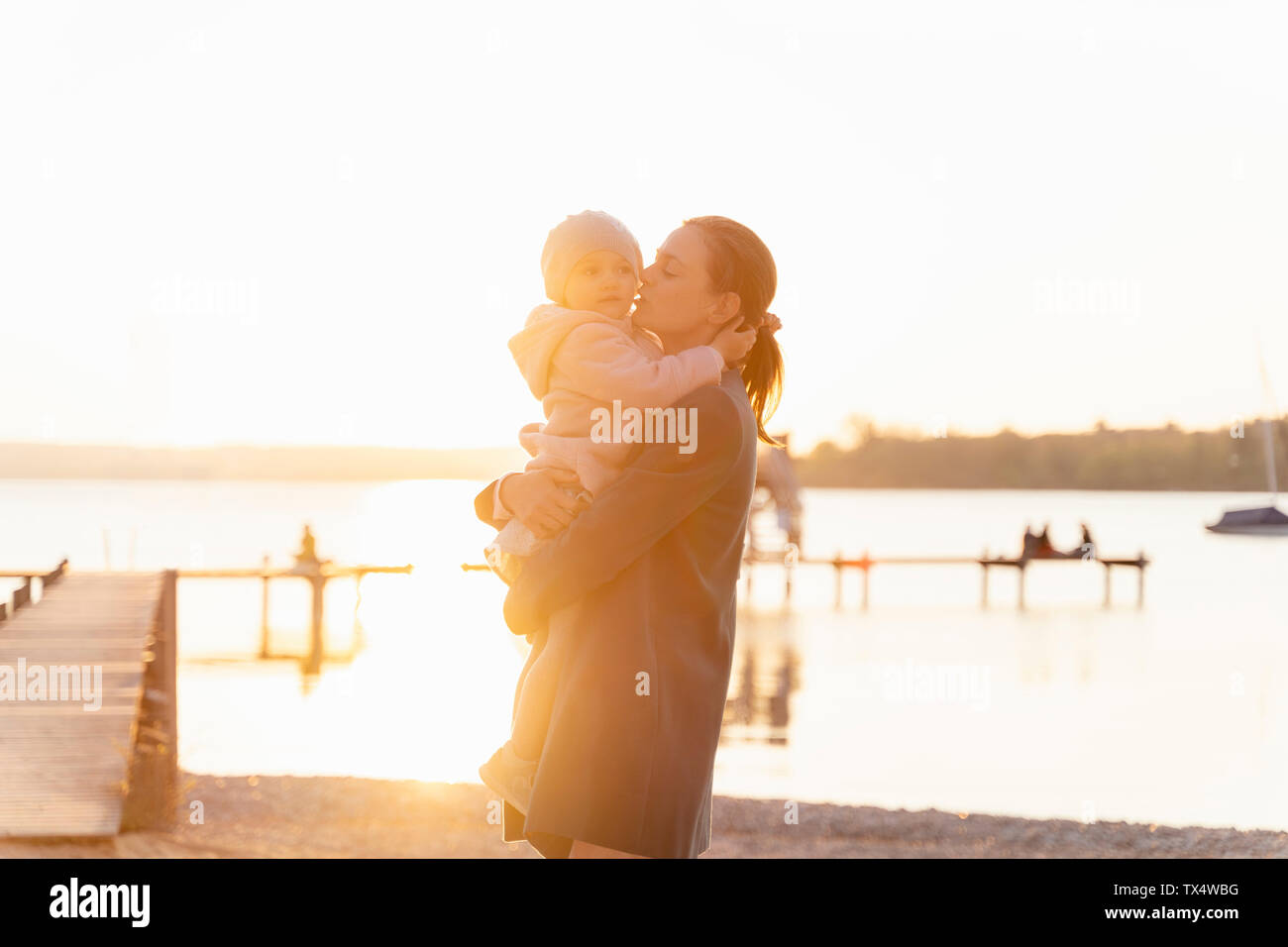 Germany, Bavaria, Herrsching, mother carrying daughter at the lakeshore at sunset Stock Photo