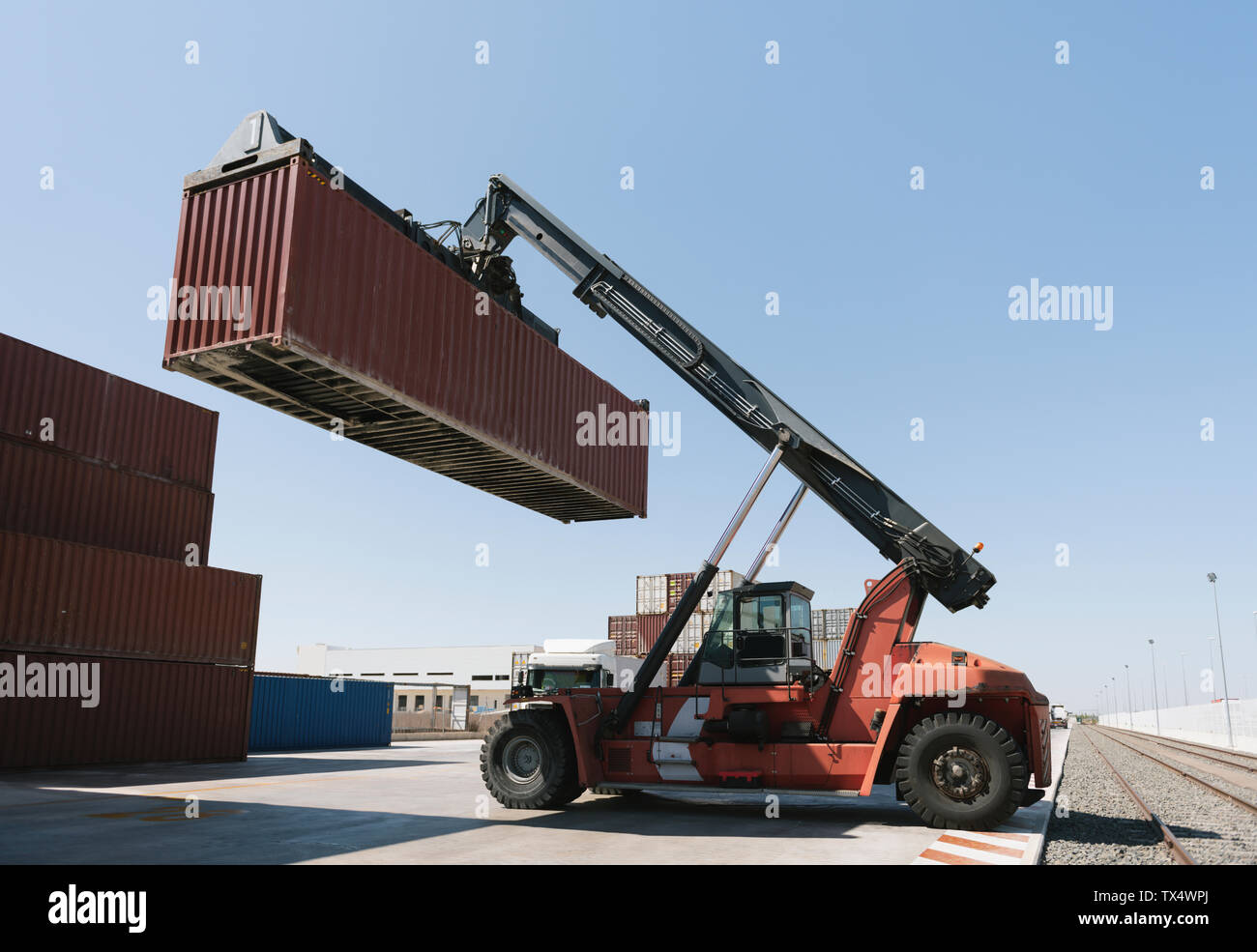 Crane lifting cargo container near railway tracks on industrial site