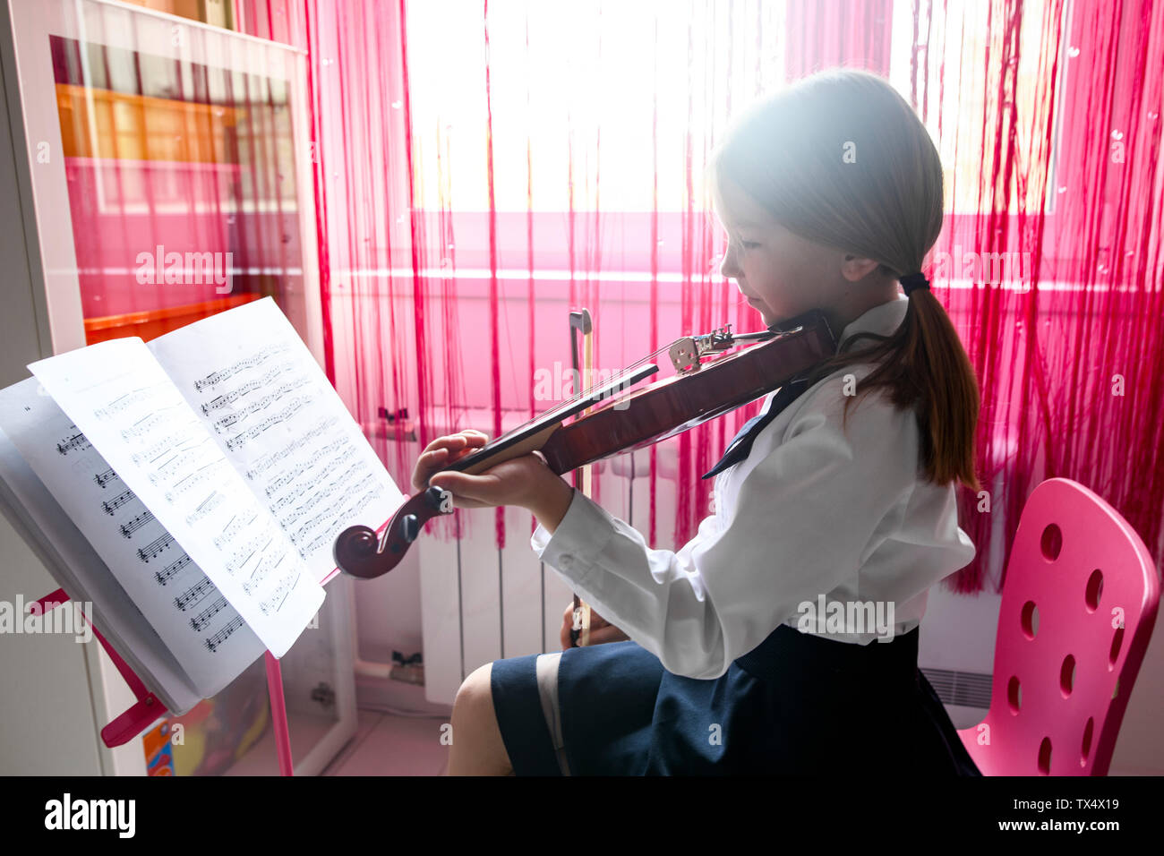 Girl sitting at the window at home playing violin Stock Photo