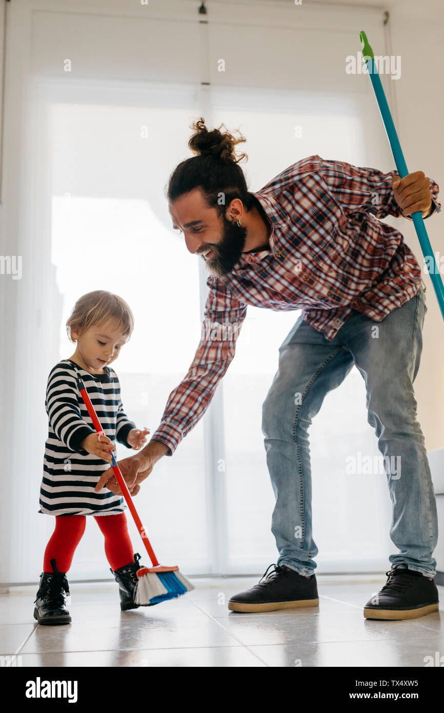Happy father and little daughter sweeping the floor of the living room at home Stock Photo