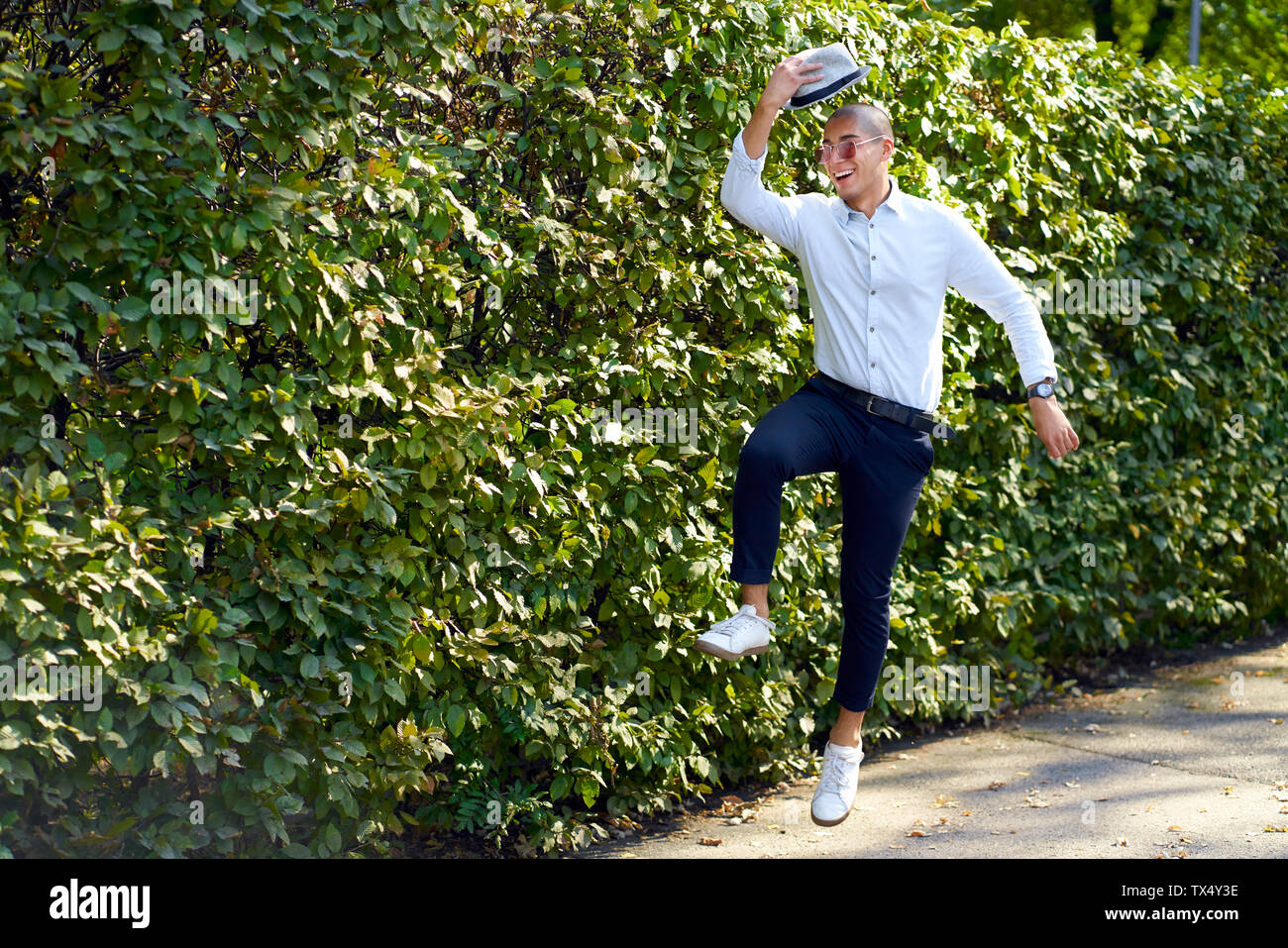 Happy young man jumping around at a hedge Stock Photo