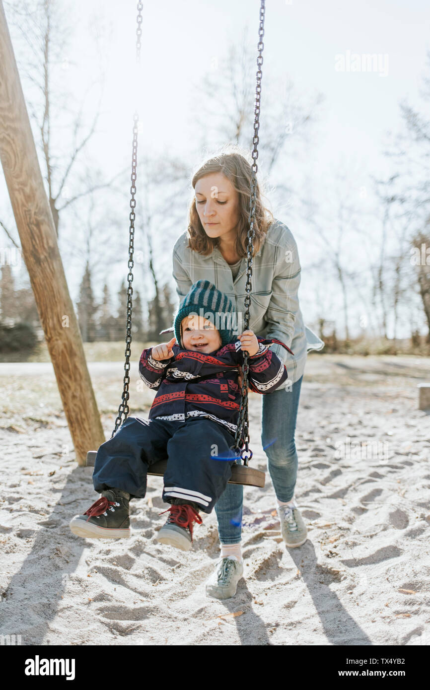 Mother with little daughter on swing on a playground Stock Photo