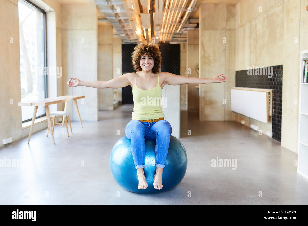 Portrait of smiling woman sitting on fitness ball in modern office Stock Photo
