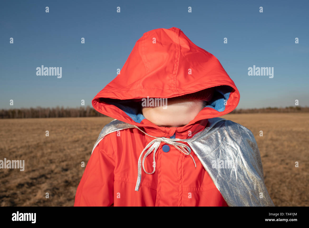 Boy dressed up as superhero in steppe landscape hiding his face in hood of his jacket Stock Photo