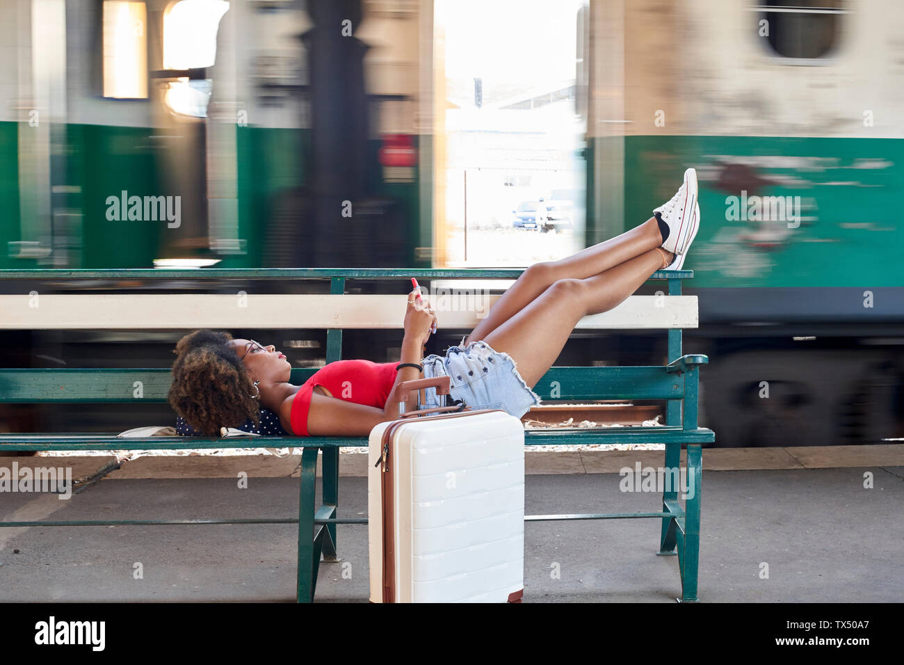 Woman with suitcase lying on a bench at the train station Stock Photo