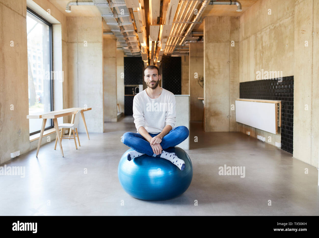 Portrait of young man sitting on fitness ball in modern office Stock Photo