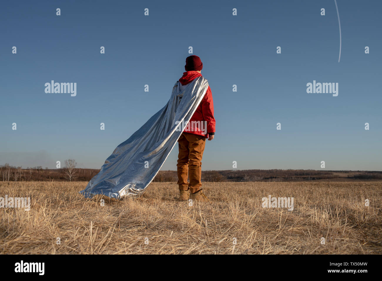 Rear view of boy dressed up as superhero looking at vapour trails in the sky Stock Photo