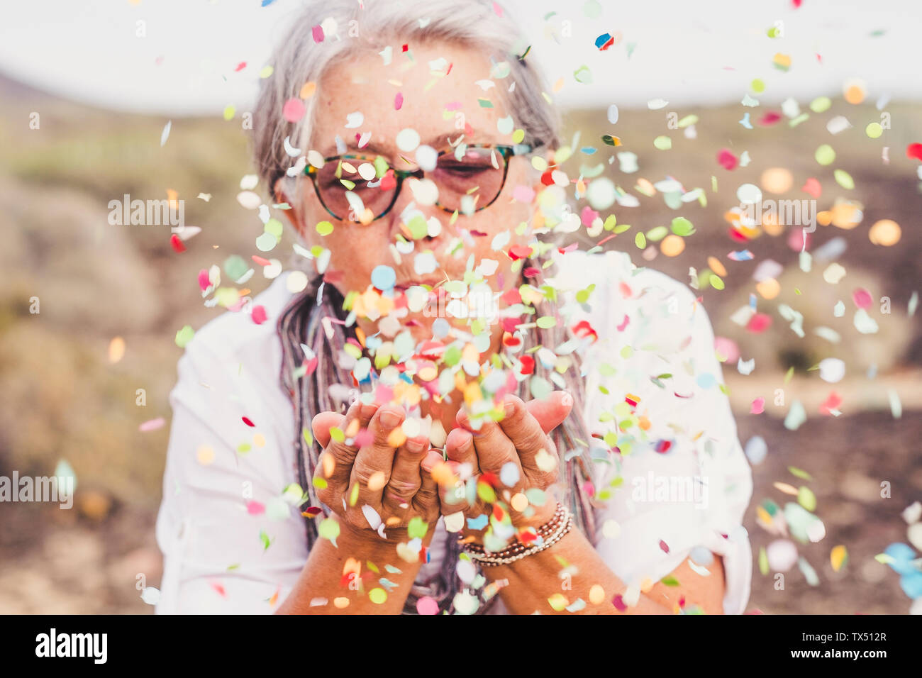 Senior woman blowing confetti outdoors Stock Photo - Alamy