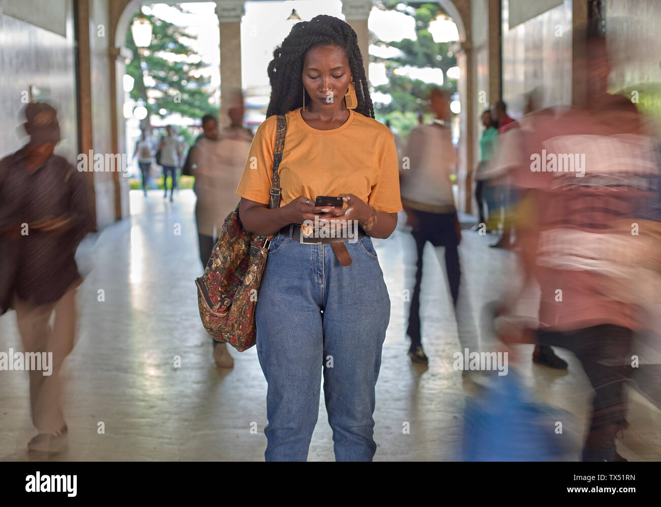 Young woman at the train station checking her phone while people passing by Stock Photo