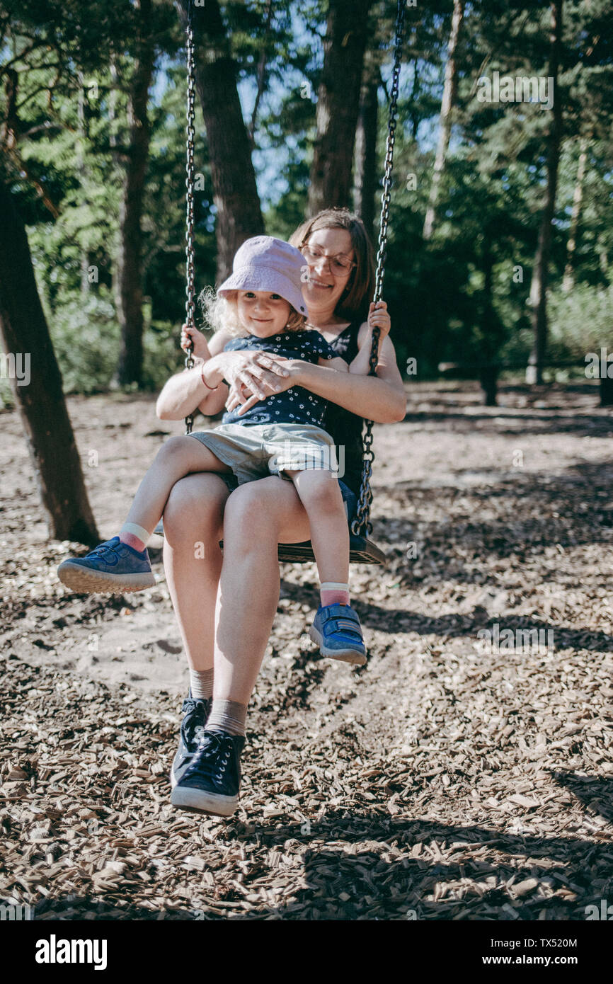 Happy mother with little daughter on swing on a playground Stock Photo